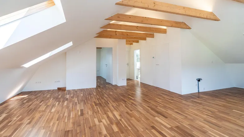 Helles Dachgeschosszimmer mit Holzbalken, Parkettboden und Dachfenstern, das viel natürliches Licht bietet.