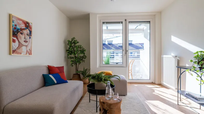 Helles Wohnzimmer mit modernem Sofa, Holzboden und Zugang zu einem Balkon.