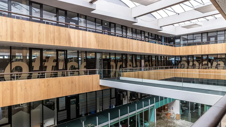 Großzügiges Atrium mit mehreren Etagen, Glasfronten und Holzverkleidungen, das viel Tageslicht hereinlässt.