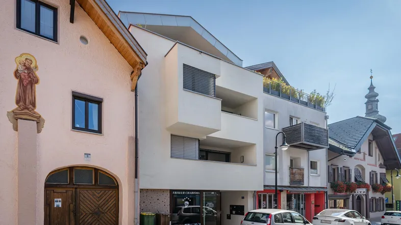 Moderne Wohngebäude mit Balkonen und Dachterrasse in einer städtischen Umgebung mit traditionellen Häusern.