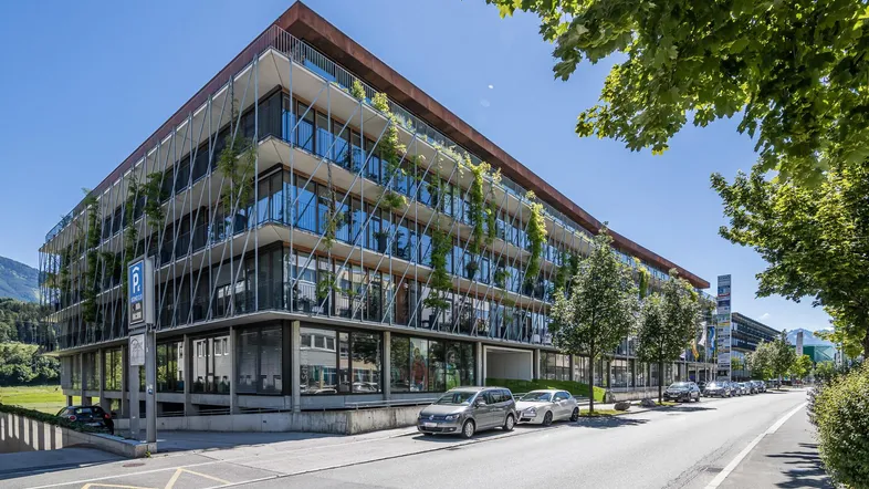 Modernes Bürogebäude mit begrünten Fassadenelementen und großen Glasflächen an einer Straße.