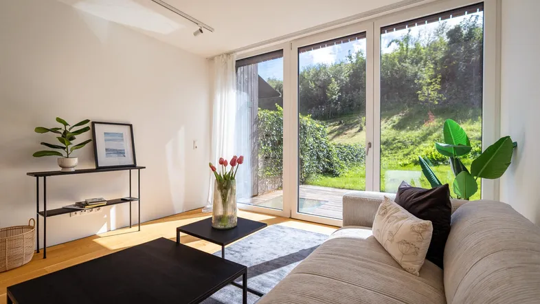 Gemütliches Wohnzimmer mit Sofa, Couchtischen und großem Fenster zum grünen Garten.