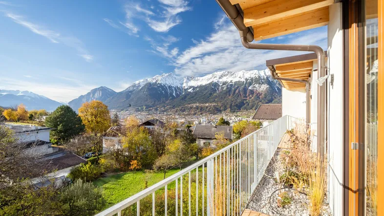 Sonniger Balkon mit Holzboden und weißem Geländer, bietet einen weiten Blick auf Berge und Stadt.