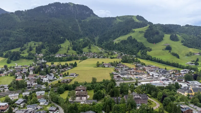 Panoramablick auf eine malerische Stadt im Tal, umgeben von grünen Bergen und Wäldern.