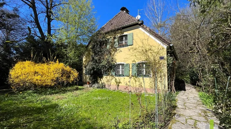 Gelbes Haus mit grünen Fensterläden und einem blühenden Garten unter blauem Himmel.