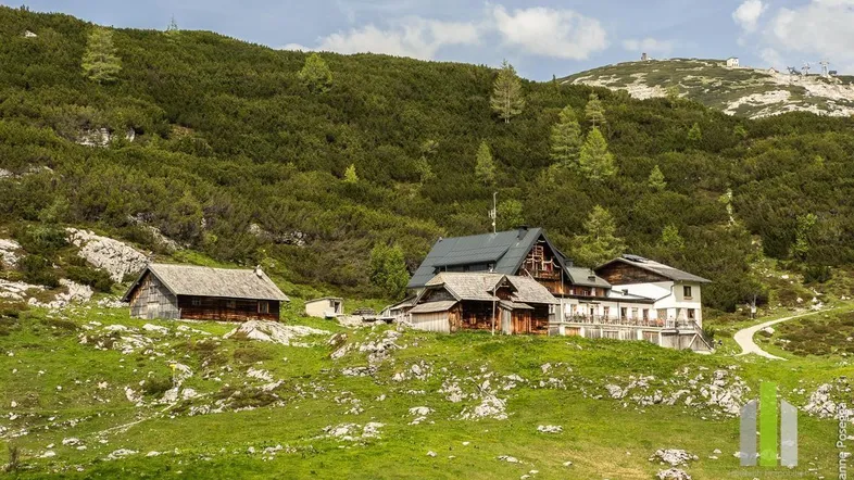 Mehrere Gebäude im traditionellen Stil eingebettet in eine grüne Berglandschaft mit felsigen Abschnitten.