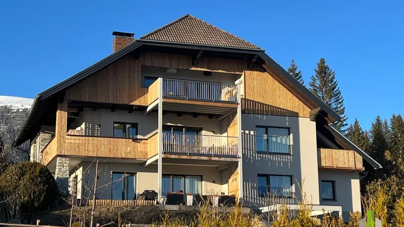 Attraktives Mehrfamilienhaus mit Holzfassade, mehreren Balkonen und Satteldach in alpiner Umgebung.
