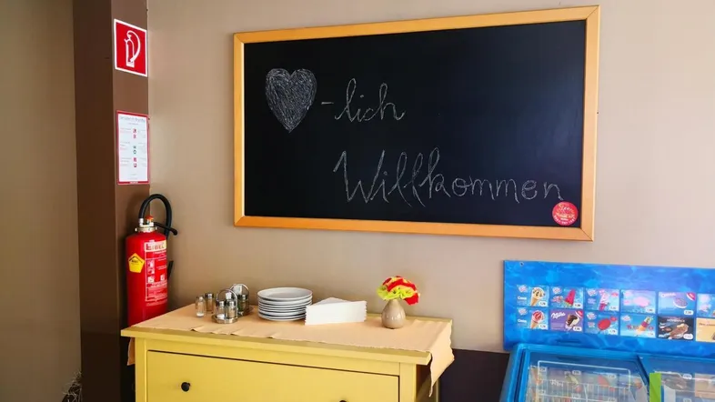 Kleiner Servicebereich mit Kreidetafel, Feuerlöscher und gelber Kommode in einem Gastronomiebetrieb.