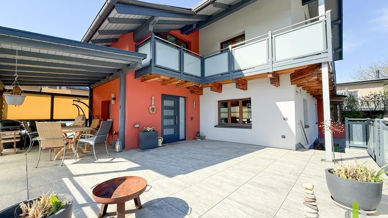 Große, sonnige Terrasse mit überdachtem Sitzbereich und modernem Balkon am Haus.