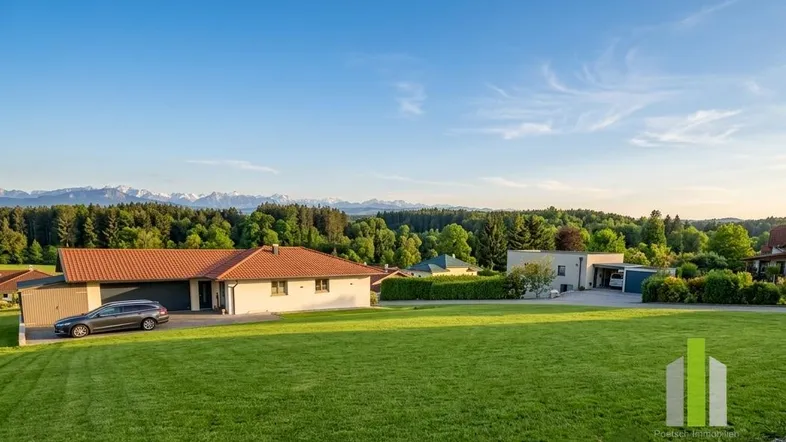 Weitläufige Grünfläche mit einem Haus im Hintergrund und Panoramablick auf die Berge.