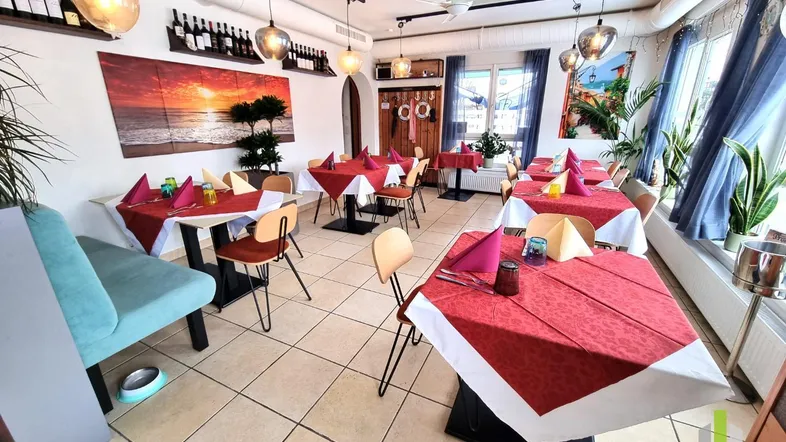 Heller Restaurantbereich mit mehreren Tischen, roten Tischdecken und maritimer Dekoration.