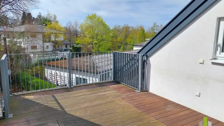Geräumige Holzterrasse mit Metallgeländer und Blick ins Grüne, ideal für entspannte Stunden im Freien.