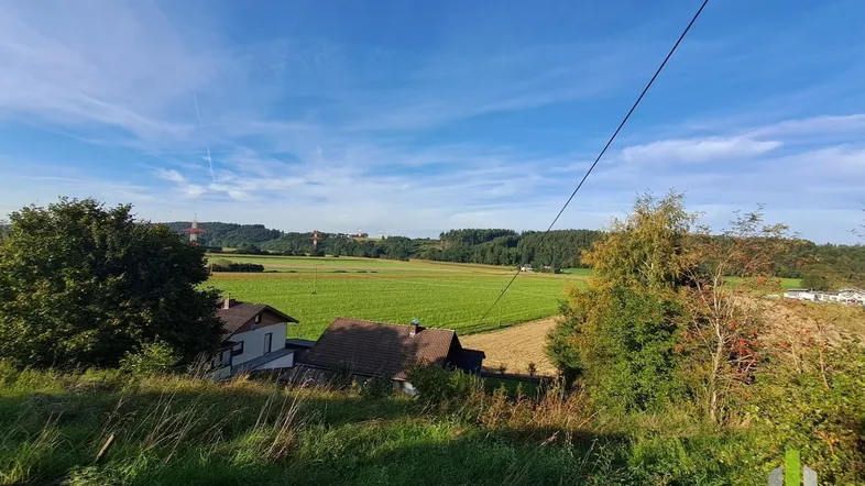 Weitläufiger Blick über grüne Felder und ländliche Umgebung unter blauem Himmel.