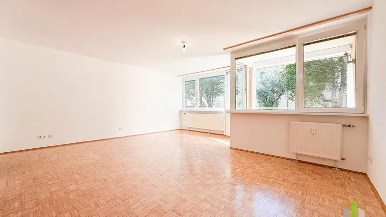 Helles Wohnzimmer mit Parkettboden und großen Fenstern, die viel Tageslicht hereinlassen.