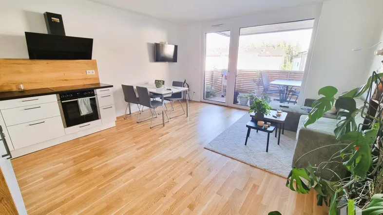 Heller offener Wohn- und Essbereich mit integrierter Küche, Holzboden und Zugang zur Terrasse.