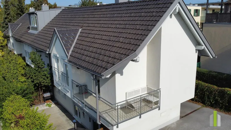 Modernes Wohnhaus mit Satteldach und Balkonen in ruhiger Wohngegend mit viel Grün.