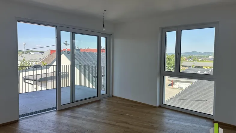 Helles Zimmer mit Holzboden, großen Schiebetüren zum Balkon und weitem Blick über die Umgebung.