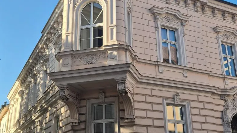 Historisches Gebäude mit aufwendig verzierter Fassade und Erker in hellem Pastellton.