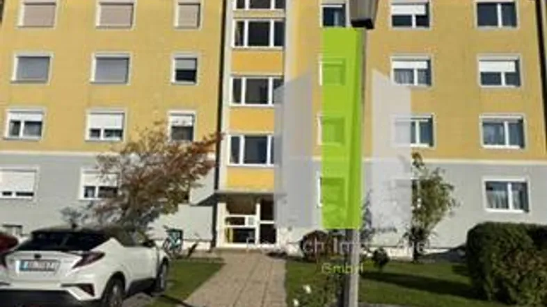 Mehrfamilienhaus mit gelber Fassade, grauen Akzenten und gepflegter Außenanlage.