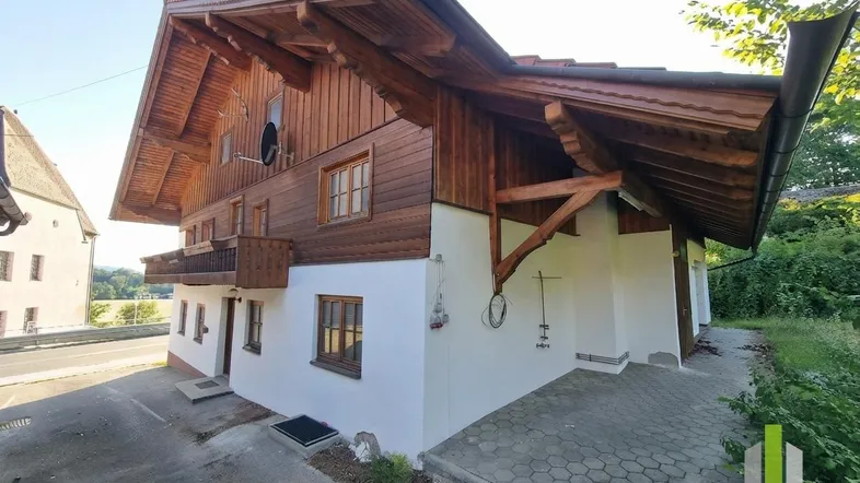 Traditionelles Haus mit Holzfassade, Satteldach und kleinem Balkon in ländlicher Umgebung.