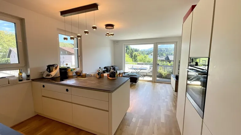 Helle offene Küche mit Kochinsel und Zugang zum Balkon, verbunden mit dem Wohnbereich.