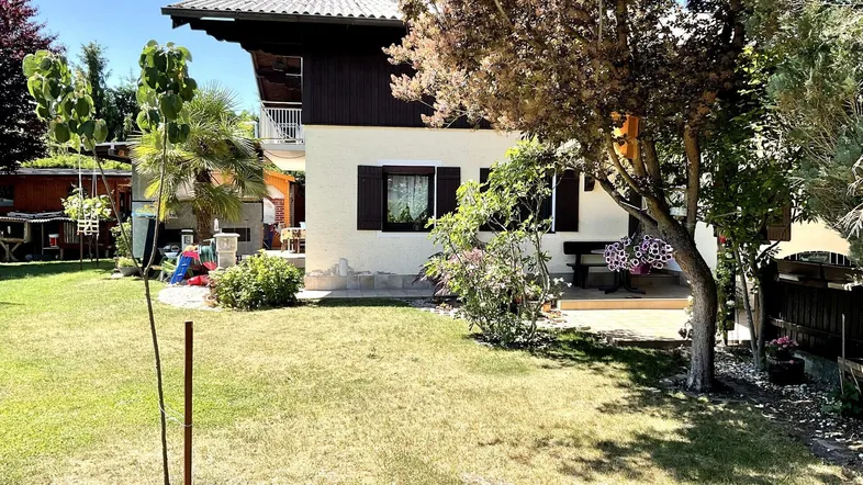 Seitenansicht des Hauses mit weitläufigem Rasen und verschiedenen Bäumen im sonnigen Garten.