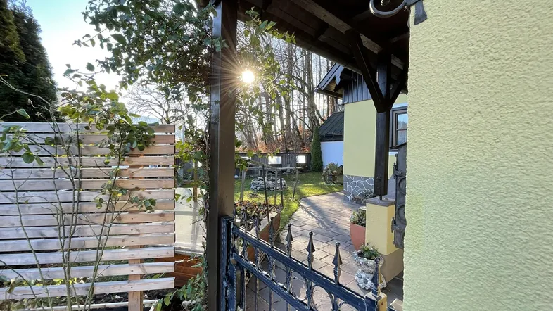 Sonniger Eingangsbereich mit schmiedeeisernem Tor, gepflastertem Weg und gepflegtem Garten.