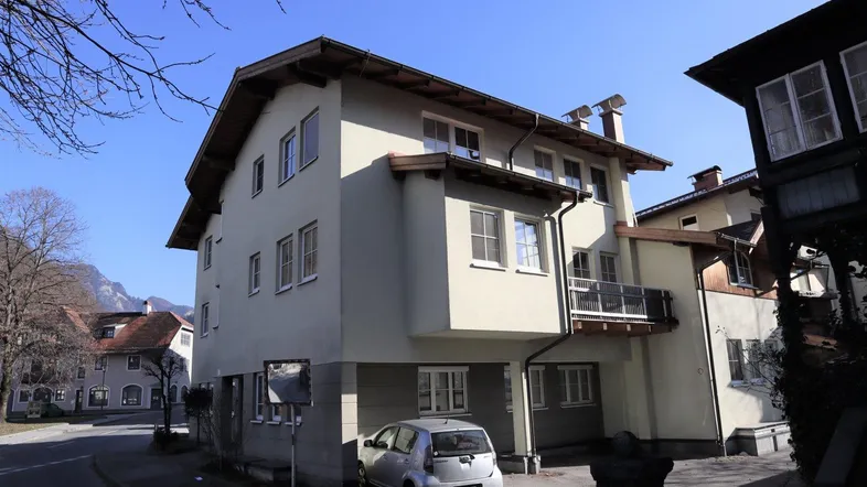 Mehrstöckiges Wohngebäude mit heller Fassade, Satteldach und kleinem Balkon in ländlicher Umgebung.