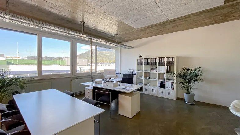 Großes, helles Büro mit moderner Einrichtung, freiliegender Decke und weitem Ausblick auf die Berge.