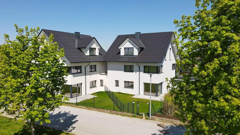 Zwei moderne Doppelhaushälften mit weißer Fassade und dunklem Satteldach in ländlicher Umgebung.