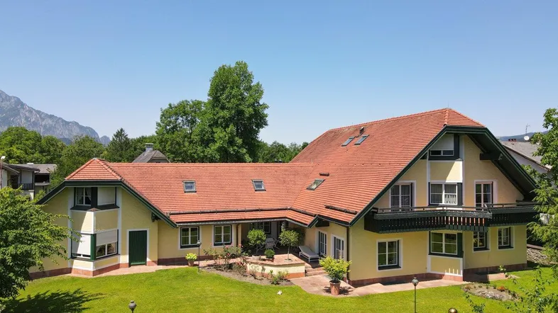 Großzügiges Haus mit gelber Fassade, rotem Satteldach und weitläufigem Garten mit Bergblick.