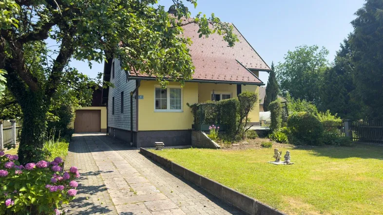 Gelbes Einfamilienhaus mit rotem Ziegeldach, gepflegtem Vorgarten und langer Auffahrt.