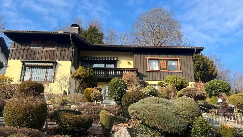 Traditionelles Haus mit Holzverkleidung und einem aufwendig gestalteten Terrassengarten unter blauem Himmel.