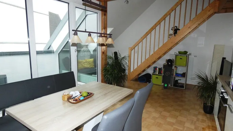 Gemütlicher Wohnbereich mit Esstisch, Holztreppe und sichtbaren Deckenbalken.