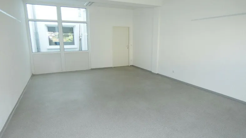 Heller, leerer Raum mit großen Fenstern und grauem Bodenbelag, ideal für Büronutzung.