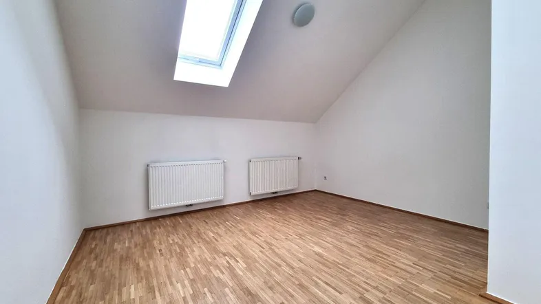 Heller Dachbodenraum mit Holzboden und Dachfenster, ideal als Schlaf- oder Wohnbereich.