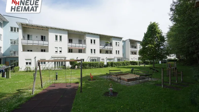 Außenansicht eines modernen Mehrfamilienhauses mit großem Gemeinschaftsgarten und Kinderspielplatz.