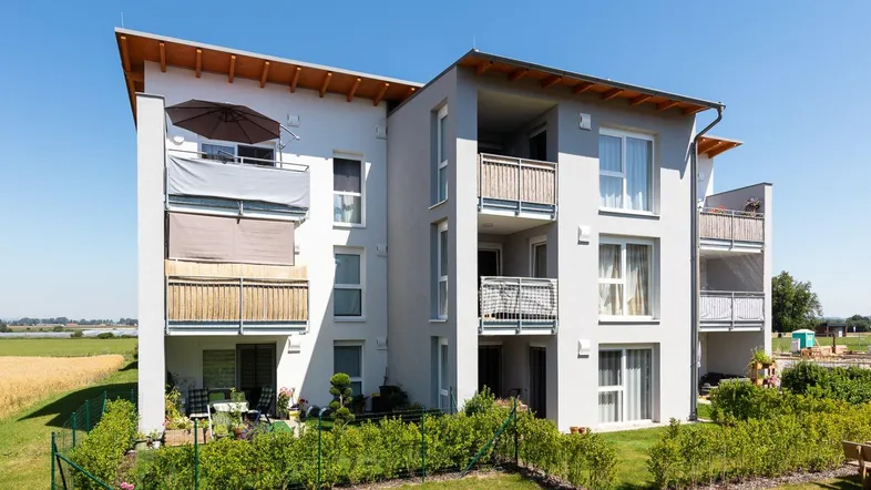 Modernes Mehrfamilienhaus mit Balkonen und Terrassen, umgeben von grüner Landschaft und Feldern.