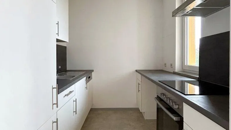 Moderne, schmale Küche mit weißen Schränken, dunklen Arbeitsplatten und Induktionskochfeld.