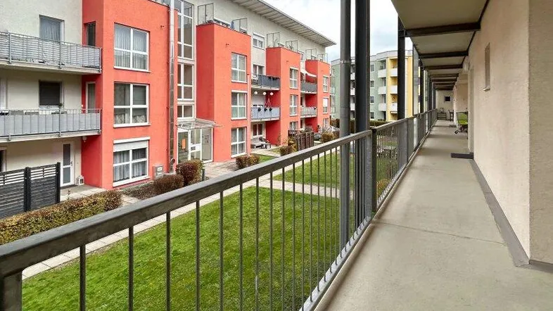 Langer Balkon mit Blick auf eine gepflegte Grünfläche und moderne Wohngebäude mit farbigen Akzenten.