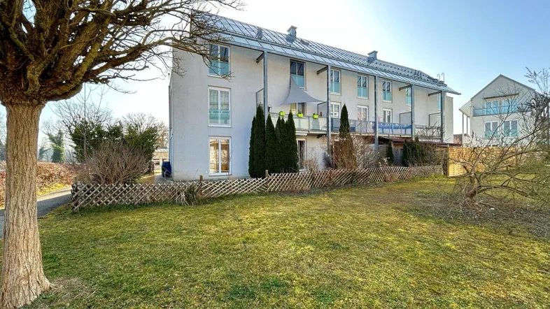 Modernes Mehrfamilienhaus mit Balkonen, Photovoltaikanlage auf dem Dach und einer gepflegten Grünfläche.