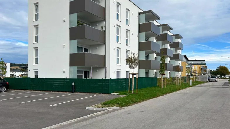 Modernes Mehrfamilienhaus mit weißer Fassade, grauen Balkonen und Außenparkplätzen.