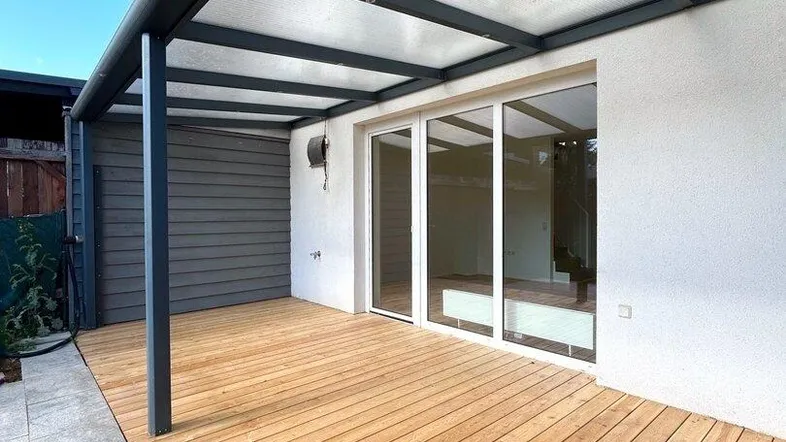 Überdachte Holzterrasse mit direktem Zugang zum Innenbereich, ideal für entspannte Stunden im Freien.