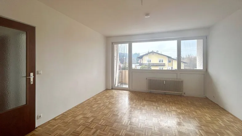 Helles Zimmer mit Parkettboden und großem Fenster mit Zugang zu einem Balkon.
