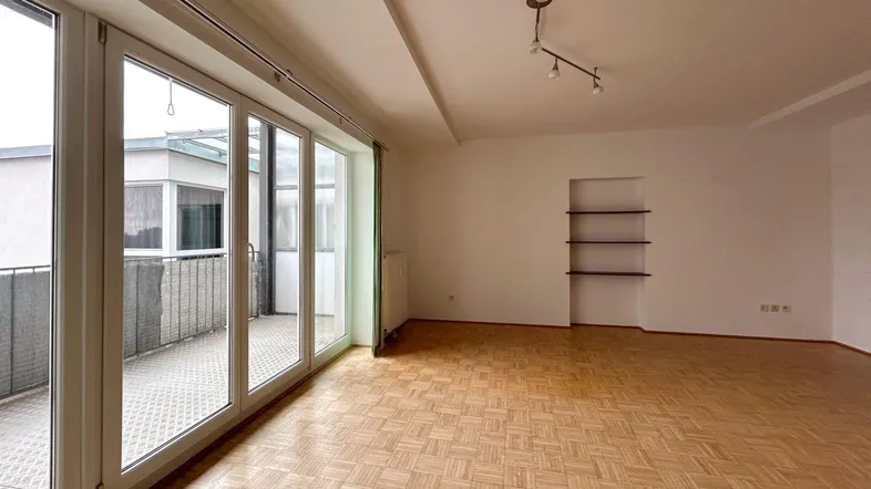 Heller, leerer Wohnraum mit Parkettboden und großzügigem Zugang zu einem Balkon.
