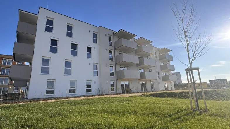 Modernes Mehrfamilienhaus mit hellen Fassaden, zahlreichen Balkonen und einer weitläufigen Grünfläche.