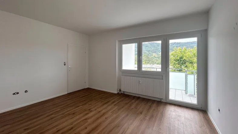 Helles Zimmer mit Laminatboden, weißen Wänden und Zugang zu einem Balkon mit Bergblick.