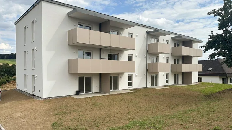 Modernes Mehrfamilienhaus mit mehreren Balkonen und einer noch unfertigen Grünfläche unter bewölktem Himmel.