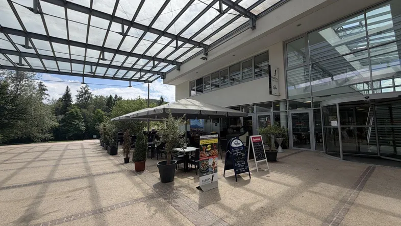 Große Außenterrasse eines Restaurants mit vielen Tischen und Sonnenschirmen unter einer Glasüberdachung.