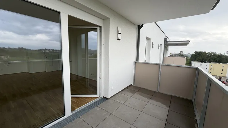 Geräumiger Balkon mit Fliesenboden und Zugang zu einem hellen Innenraum.